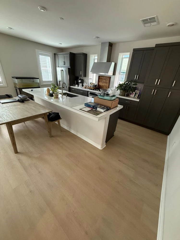 Modern kitchen with light-colored plank flooring, dark cabinetry, and a large white island, showcasing a clean and contemporary interior.