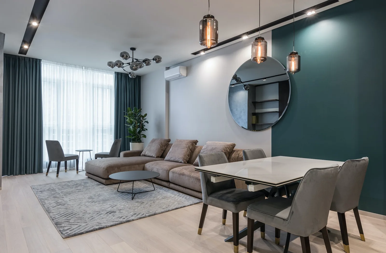 Living and dining space with a deep teal wall over light plank flooring Living and dining space with a deep teal wall over light plank flooring